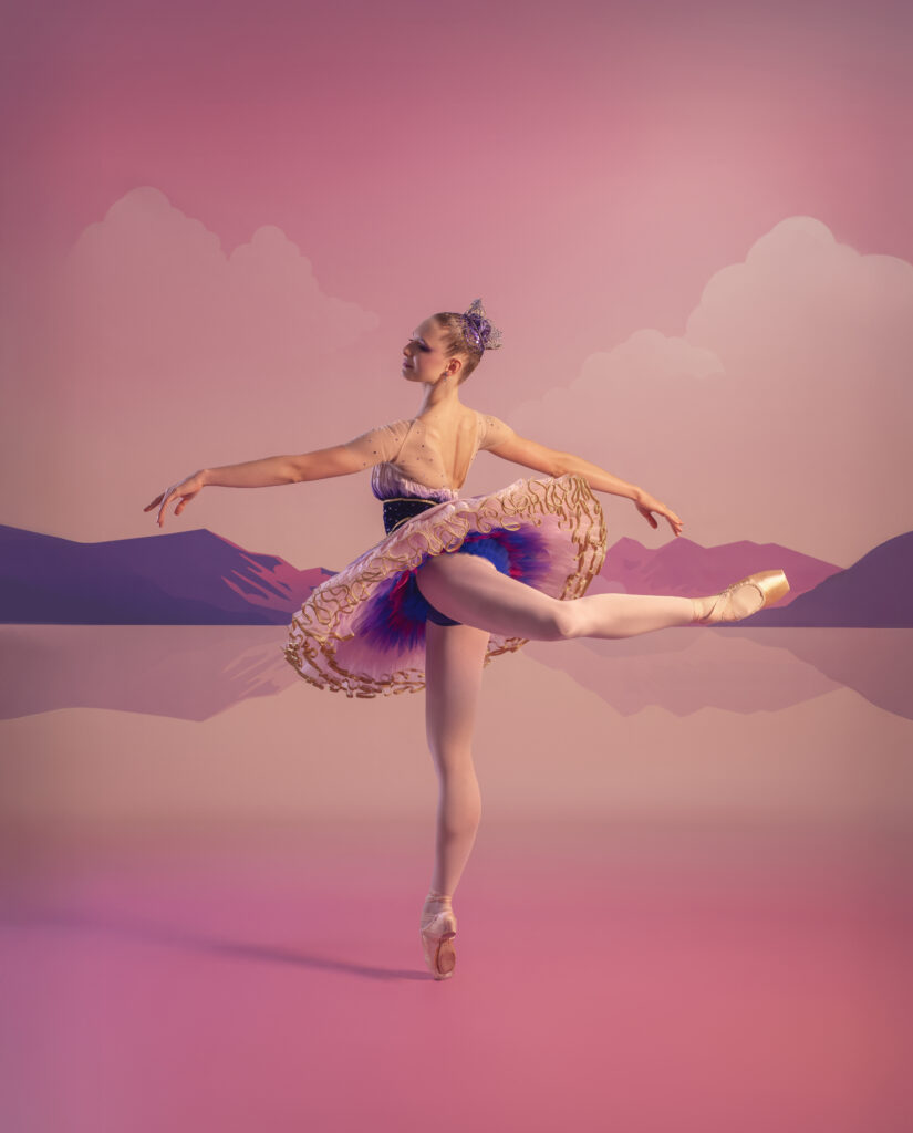 A ballerina in a tutu dances en pointe with one leg extended behind her, set against a pastel-colored background with mountains and clouds.