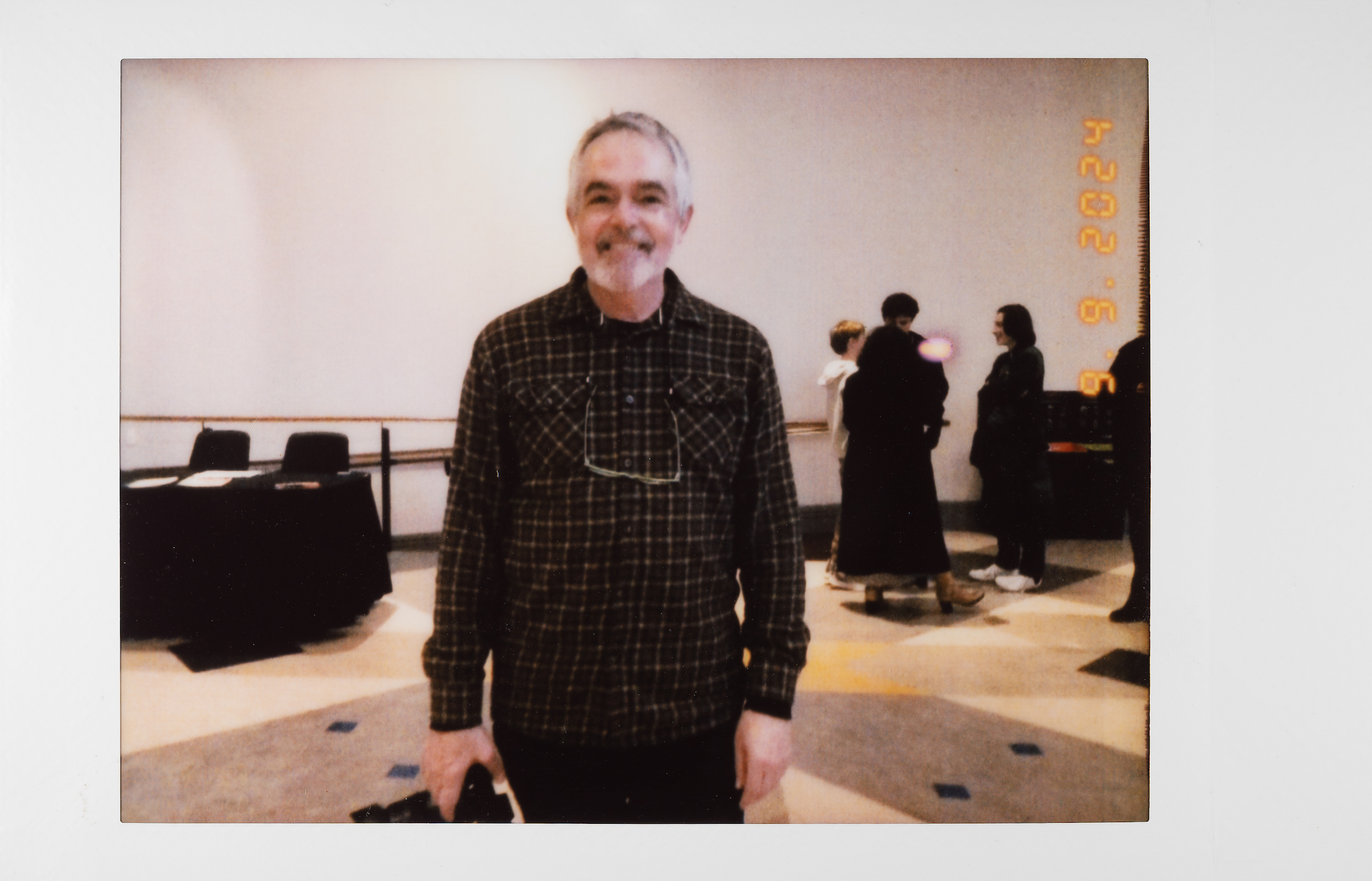 Stephen, A man in a plaid shirt smiles at the camera while standing indoors. In the background, several people are gathered and talking near a table. The date 2024.5.9 appears in orange text on the right side.